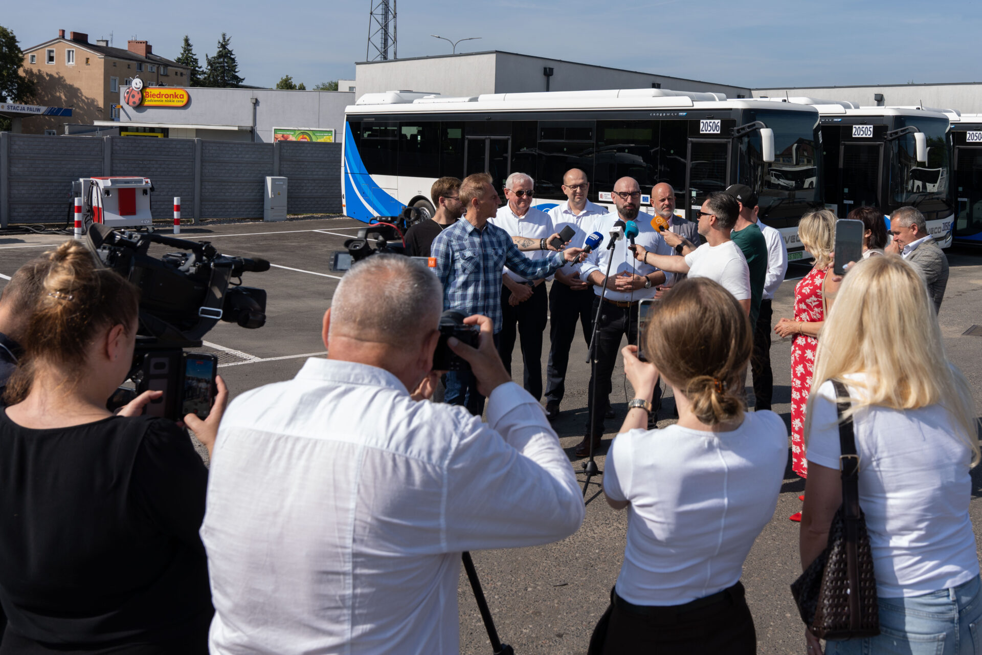 Konferencja prasowa Powiatu Słupskiego i PKS Słupsk SA. Przemawia Starosta Powiatu Słupskiego Paweł Lisowski, na tle nowo zakupionych autobusów elektrycznych. Dookoła dziennikarze z kamerami, mikrofonami i aparatami.